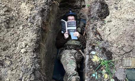 Боєць ЗСУ читає між боями в окопі англомовну книжку. Фото дня